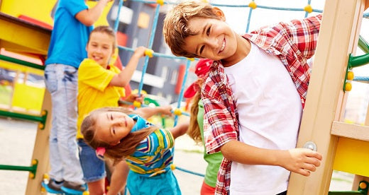 Children playing actively on an outdoor playground, smiling and engaging with climbing structures and slides, promoting social interaction and physical development.